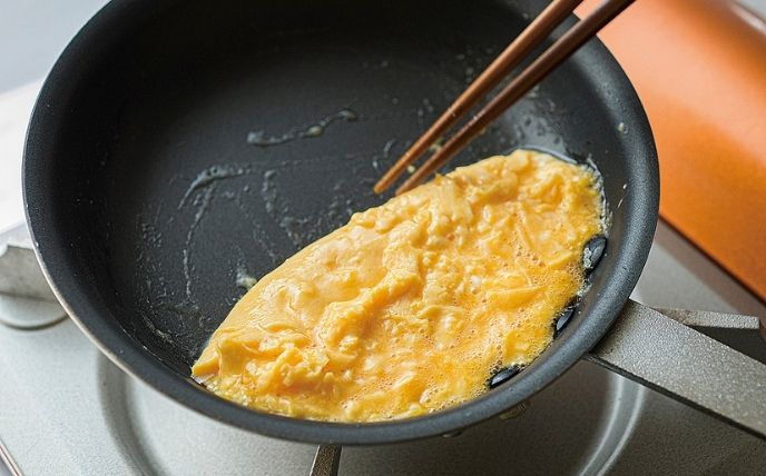 フライパンの縁を使って形を整える
コンロにフライパンを戻し、弱火でフライパンを傾けながら菜箸で端から巻き込んで形を整えていきます。フライパンの縁に卵を寄せて焼き固め、きれいな面が上になるようお皿に返して盛り付けます。