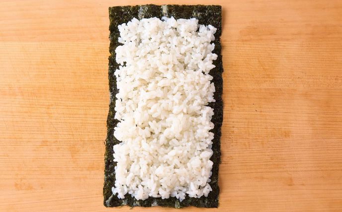 半分に切ったのりを縦に置く。奥は1cm、左右と手前は0.5cmを残して、のりに酢飯100gを敷き詰める。